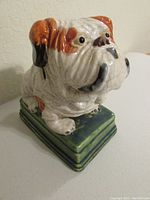 Side-angle view of porcelain bulldog figurine showing glaze crazing, orange and black accents, and green base.