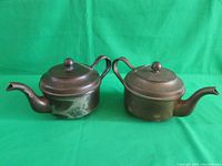 Pair of two vintage teapots with curved spouts and loop handles, showing significant patina and wear.