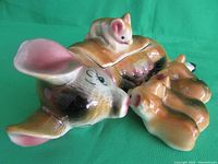 Side angle photograph showing the mother pig lying down with piglet lid atop, four detached piglets visible to the right.