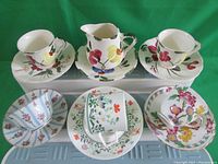 Top view of all cups, saucers and creamer jug showing floral and fruit designs of each set.