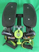 Top and front view of black stepper with textured foot pedals and yellow-green digital step counter.