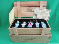 Five Christmas glass ornaments displayed inside a wooden crate box with a certificate of authenticity.