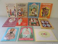 Full lot of 11 vintage paper doll books arranged in two rows, showing variety of themes and colorful illustrated covers.