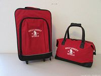 Full view of red rolling suitcase and red weekender bag side by side, both with Walt Disney World 1971 Mickey Mouse logo embroidered in white.