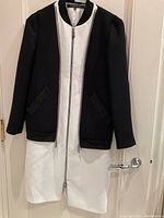 Black and white Barbara Bui dress combined with black jacket with zipper front, hanging on hanger against door.