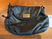 Front view of black pebbled leather bag with curved flap and gold-tone nameplate