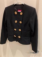 Front view of black double-breasted cropped jacket hanging on a door