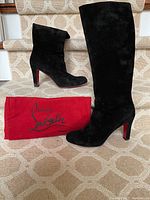 Two black suede knee-high boots displayed on stairs alongside red dust bag