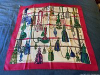 Full view of square silk scarf laid flat showing red border and tassel print