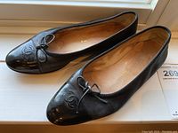 Pair of black Chanel ballet flats shown from side/top angle on windowsill