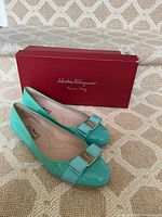 Pair of mint green patent leather flats next to red Salvatore Ferragamo box on patterned carpet