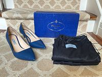 Pair of blue Prada pumps with pointed toes, original box, and two black dust bags arranged on stair