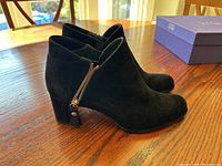 Side view of left and right black suede ankle boots on wooden table showing gold side zipper and block heels