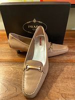 Front and side view of the pair of tan leather Prada loafers with box in background