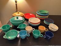 Full lot view showing all plates, bowls, mugs, creamer and covered casserole on black surface