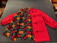 Full view of coat laid flat showing red exterior and folded interior print