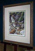 Angled full view of framed print on easel against dark background