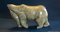 Side view of green soapstone polar bear figurine carrying a seal on its belly.