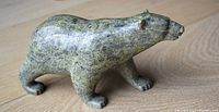 Left side profile of green mottled soapstone polar bear sculpture on wood surface.