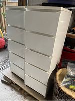 Two white Ikea Malm dressers side by side showing their fronts and sides in a storage area.