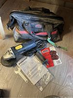 Photo showing a Mastercraft angle grinder, black and red Jobmate toolbag, metal handle, wrench, and instruction manual on a wooden floor.