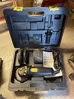 Open case showing Mastercraft angle grinder with extra grinding wheels, power cord, auxiliary handle, and manual organized inside.
