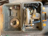 Open case showing Maximum corded circular saw inside with two circular saw blades and orange plastic accessories.