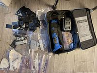 Top-down view of the cordless multitool with battery, charger, multiple sanding and cutting attachments, sandpaper in Ziploc bags, and two carrying bags.
