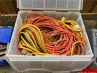 Top-down view inside one plastic bin showing a mixture of mostly yellow and orange outdoor extension cords coiled and packed tightly.