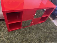 Front view of glossy red shelving unit with two closed mirrored doors in center compartments and two red doors on the sides, with three open square compartments on the sides.