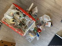 Plastic bin filled with assorted hardware including various screws, knobs, hooks, and small parts in plastic bags