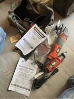 View of both power tools, oscillating multitool and rotary tool, with instruction manuals and attachments, on wood floor.