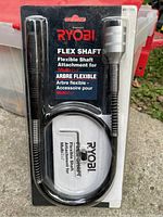 Photo of the Ryobi Flex Shaft attachment in its original packaging, showing the flexible black shaft and metal ends, packaged on Ryobi branded backing card.