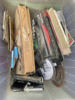 Top-down photo of bin containing assorted saw blades, several powered staple tools including a Craftsman, and unopened staple boxes