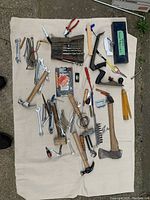 Top view of assorted hand tools including wrenches, hammers, pliers, measuring tools, and small hand tools laid out on a beige cloth.