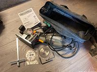Photo showing the Rockwell Versacut wall saw with cord, instruction manual, measuring guide, two circular saw blades, and two Allen wrenches all laid out on floor.