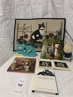 Photo showing all items in the lot including cat tapestry, decorative mirror, wood cat figures, framed tiles, and books.