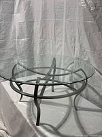 Full view of the round glass coffee table showing glass top and metal base with curved legs.