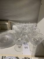 Photo showing six crystal stemmed glasses and six matching cut crystal plates arranged on a white surface.