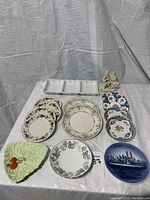Photo showing full collection of plates, figurine and serving dish on white tablecloth, arranged in groups.