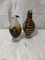 Photo showing two solid heavy glass bird figurines side by side on a white surface with plain background, highlighting their colors, shapes, and hollow cutouts.