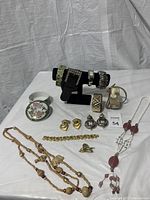 Photo of vintage jewelry lot items arranged on white cloth including necklaces, clip-on earrings, various bracelets and a trinket box.