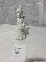 Full view of white ceramic angel figurine holding candle holder, standing on flat surface with visible folds in gown and wing detail.