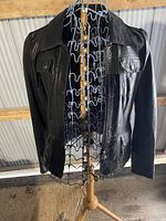 Black leather bomber jacket on a stand, front view showing collar, chest pockets with buttons, full zipper, and long sleeves.