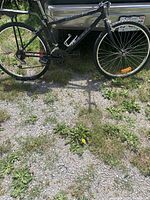 Full side view of black Niji Squall mountain bike leaning against a car, showing frame, wheels, tires, pedals, gears, rack, and brakes.