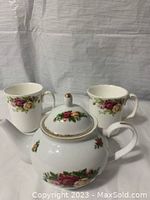 Front view of small Royal Albert porcelain teapot with floral rose pattern and gold trim, shown with two matching coffee/tea mugs