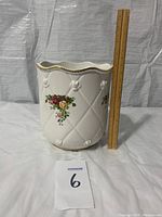 Full view of cream-colored ceramic waste basket / planter with embossed quilt pattern, raised roses, and Old Country Roses floral design. Ruler shown for approximate size (about 10 inches tall).