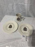Photo showing Queen Elizabeth II commemorative mug and two silver jubilee plates, arranged on a table against a white background.