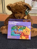 Rus teddy bear with tag sitting behind the sealed Disney Winnie the Pooh playing cards box showing front of package with Pooh and Tigger illustration.