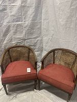 Full view of two wooden cane back chairs with burgundy pink seat cushions.